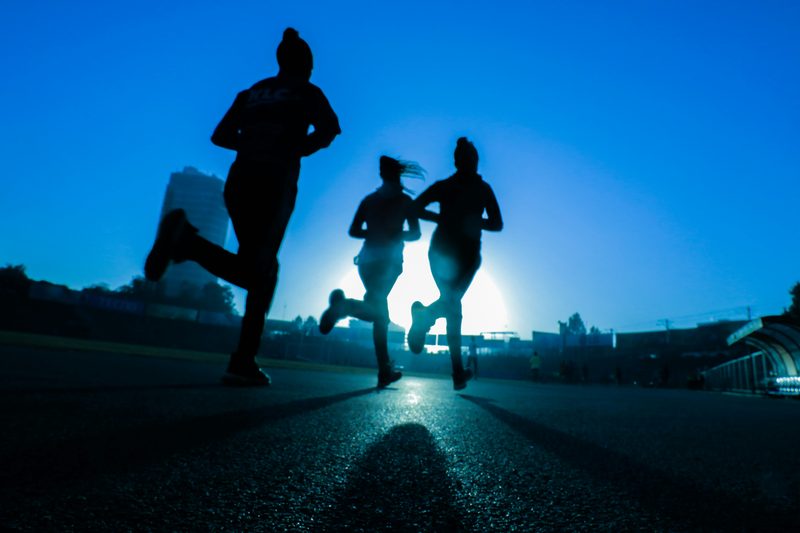 Three runners in silhouette running toward the rising sun